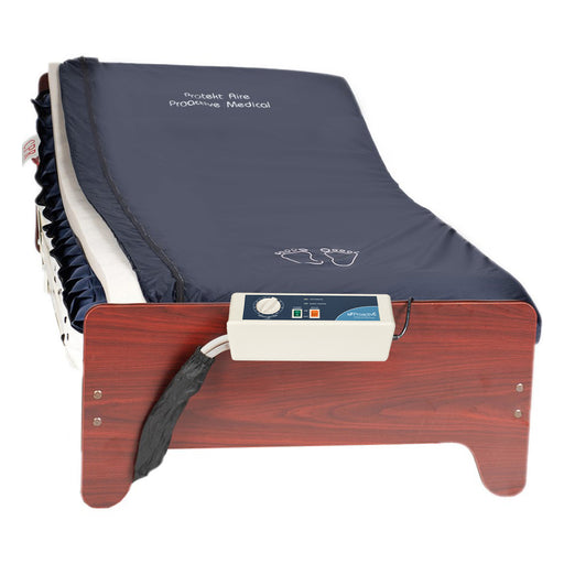 Full view of the Proactive Protekt 1st Defense mattress system on a wooden bed frame. The dark blue mattress cover has "Protekt Aire Proactive Medical" printed on it and the Protekt Aire 2000/3000 pump is visibly connected to the foot of the bed