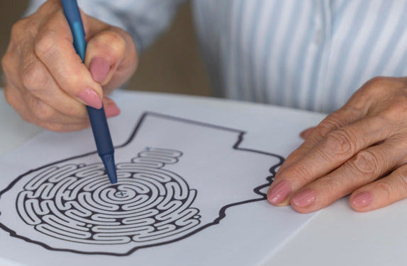 Senior woman coloring a black and white maze design on paper with a blue pen. Photo by Freepik.