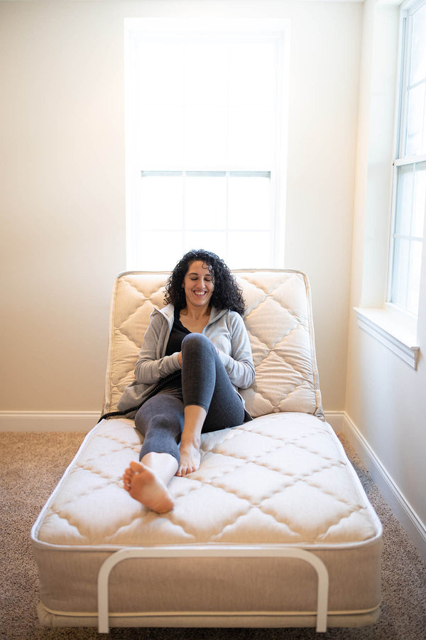 A woman sits upright and smiles while relaxing on the Flexabed Value-Flex adjustable bed. The customizable bed is raised in a seated position.