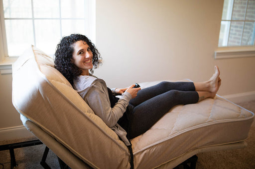 A woman with curly hair smiles directly at the camera while comfortably reclined on the customizable Flexabed Value-Flex adjustable bed