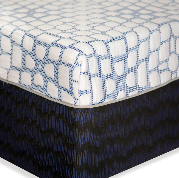 A close-up of the mattress corner showing the transition from the white tiled top to the dark navy side panel, separated by a clean grey piping.