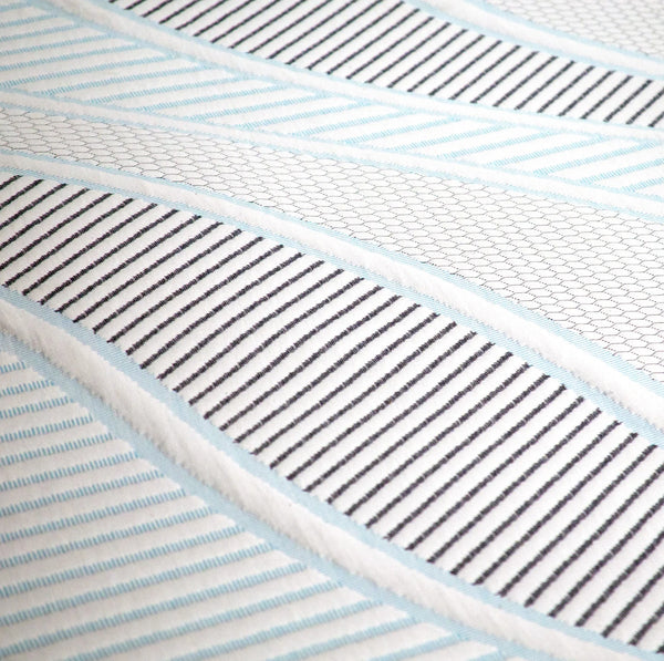 A macro shot of the mattress surface fabric, revealing a sophisticated mix of textures: light blue accents, grey honeycomb hexagonal knits, and sharp diagonal charcoal stripes.