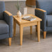 A light natural wood square side table with four legs, styled between two blue upholstered armchairs in a modern indoor setting.