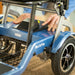 Close-up of hands removing the Journey So Lite lightweight folding power scooter's battery pack, showing the easy battery removal feature and blue scooter frame.