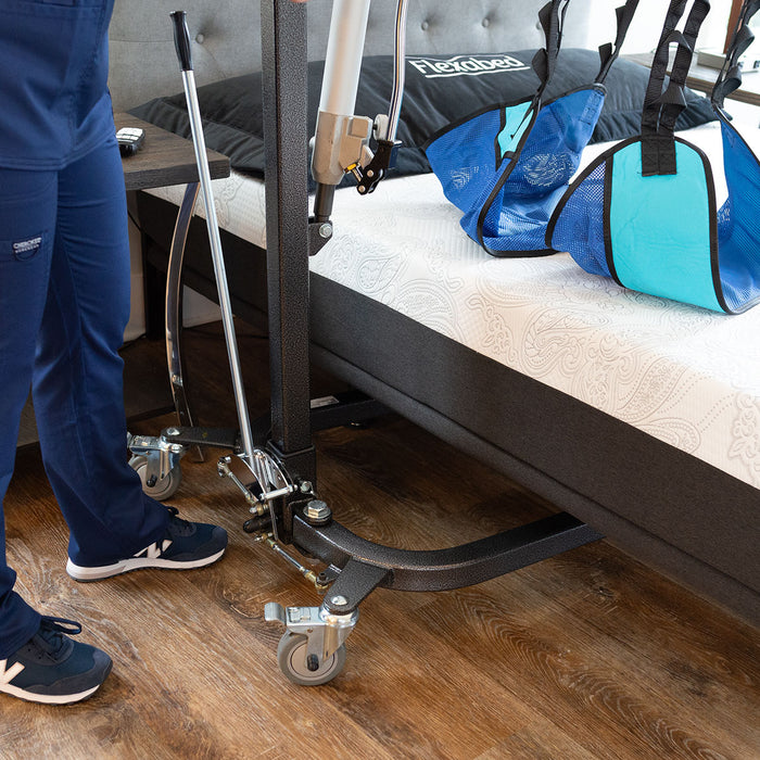 Close-up of a caregiver operating a Hoyer lift beside a Flexabed Hi-Low adjustable bed with optional mattress, showing mobility assistance equipment