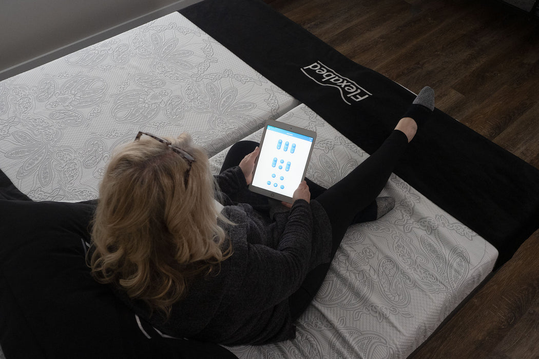 Woman sitting on a Flexabed Hi-Low adjustable bed with optional mattress while using the Okin SmartBed app on a tablet to adjust the bed 