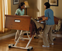 Two caregivers assisting a patient on the UltraCare XT bed system. The bed is tilted into the Gravity Assist position, showing the bed frame lifting and tilting for easier patient repositioning.