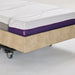 A close-up shot of the foot of the bed, highlighting the seamless integration of the extra-long bolster extension. The bolster features a matching white patterned top and a distinctive purple side band with the "icare" logo.