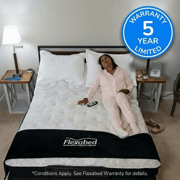 Woman sitting on a Flexabed Hi-Low adjustable bed with optional mattress and remote control on the bed, showing the Flexabed logo on the blanket