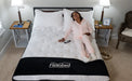 Woman sitting on a Flexabed Hi-Low adjustable bed with optional mattress and remote control on the bed, showing the Flexabed logo on the blanket