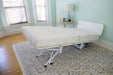 The Bariatric Hospital Bed with Trendelenburg - Transfermaster Valiant features an adjustable raised backrest and offers comfortable medical-grade positioning in a light blue room with hardwood floors, patterned rug, windows, and a small round table.