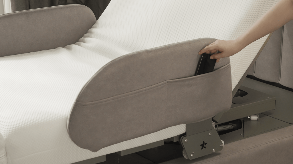 A hand places a smartphone into the side pocket of the gray Starsleep Orin Rotating Bed, which features a white mattress.