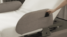 A hand places a smartphone into the side pocket of the gray Starsleep Orin Rotating Bed, which features a white mattress.