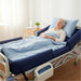 Elderly patient comfortably resting on the Protekt Aire 8600AB air mattress with raised bolsters, connected to the Protekt Aire 8000 pump