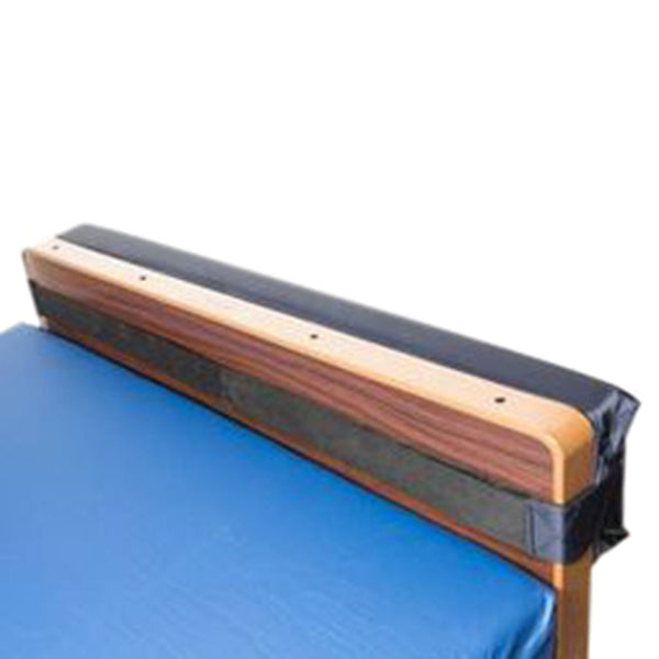An isolated close-up of a Protekt Wall Guard, a black padded strip with Velcro straps wrapped around the top edge of a wooden bed headboard, intended to protect walls.