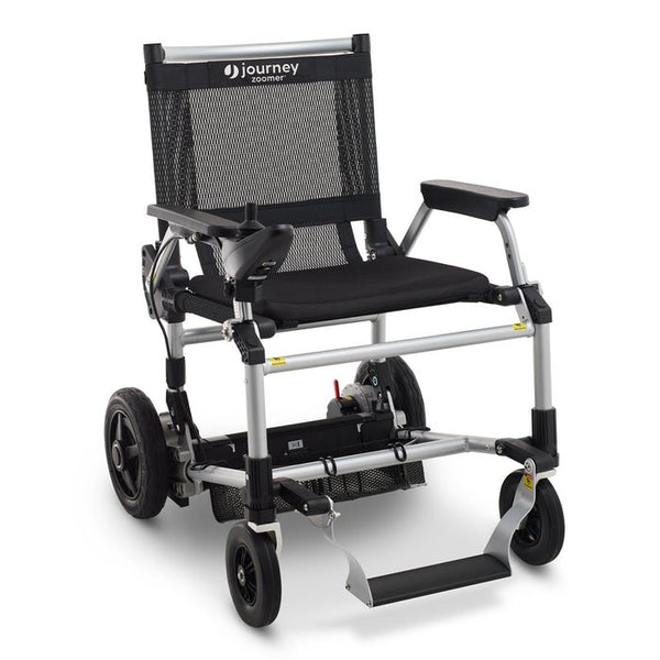 A studio shot of the standard black Zoomer Power Chair shown from a three-quarter front angle. The mesh backrest and padded seat are visible, along with the under-seat storage basket and the patented floating footrest.