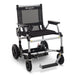 A studio shot of the standard black Zoomer Power Chair shown from a three-quarter front angle. The mesh backrest and padded seat are visible, along with the under-seat storage basket and the patented floating footrest.