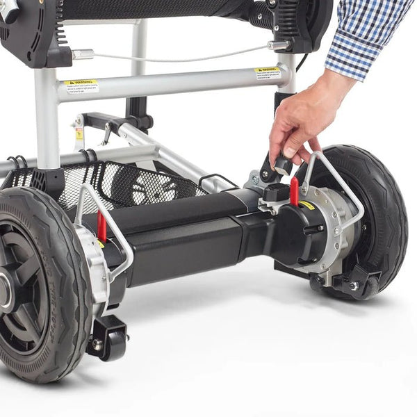 A close-up view of a person’s hand connecting a power plug into the rear motor assembly of the Zoomer chair. The heavy-duty rear wheels and black motor housing are visible.