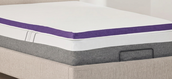 A close-up, side-angle view of a white ActiveX mattress overlay placed on top of a mattress, featuring a distinct dark purple fabric border around the edge of the overlay.