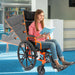 A teenage girl reading a book in an orange Ziggo Pro reclining wheelchair; a translucent overlay shows the backrest's ability to recline into a flat position for rest.