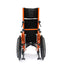 Rear view of an orange Ziggo Pro wheelchair showing the back stabilizer bar, attendant hand brakes on the push handles, and the rear anti-tippers.