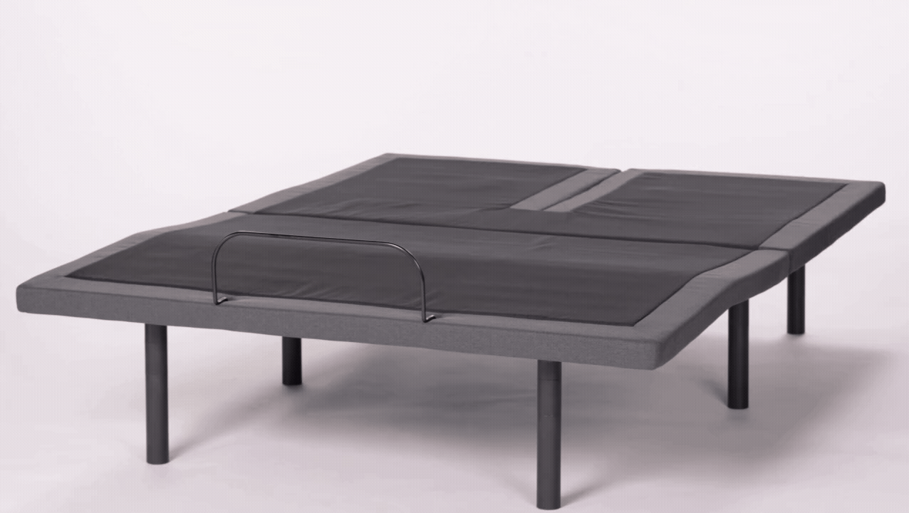 The Customatic Synergy adjustable bed frame with a split-head design. One side of the head section independently inclines to a sitting position while the other side remains flat, illustrating personalized comfort for partners.