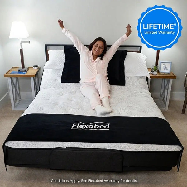 Person sitting on a Flexabed Premier adjustable bed with arms raised, showing a home bedroom setup and highlighting the lifetime limited warranty.
