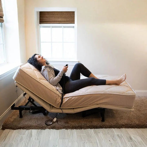 Woman reclining on a Flexabed Value-Flex adjustable bed using a wired remote, showing head and foot elevation in a home care bedroom