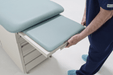A close-up of a healthcare professional extending the padded leg rest extension from the foot of the Hausted 4200 Exam Table. The extension slides out smoothly to provide additional surface area for supine examinations.