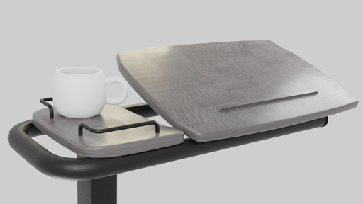 A close-up view of the Icare over bed table top, showing the wood-grain tilting surface slightly elevated and a gray side tray holding a white mug. The view is from the side, emphasizing the tilting mechanism.