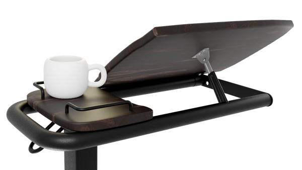 A close-up, side-angle view of the Icare over bed table, highlighting the tilting mechanism underneath the wood-grain surface. A white mug sits on the adjacent fixed side tray.