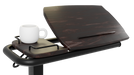 A close-up, side-angle view of the Icare over-bed table, showing the wood-grain surface tilted upwards with a book-rest groove. A white mug sits on the adjacent fixed side tray.