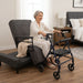 The Independence Bed in upright chair position with elderly woman reaching for walker, demonstrating sit-to-stand transfer