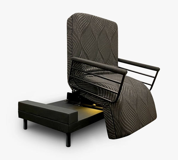 The UPbed Independence Adjustable Bed for Seniors by Journey Health features a black patterned upholstery, raised backrest, mechanical lift system, and short black legs, resembling a rotating bed. Shown against a plain white background.