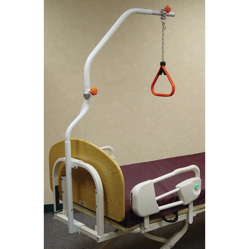 Full Joerns trapeze set attached to a hospital bed. A white metal arch extends over the bed with an adjustable chain and a red triangular handle hanging down. The bed has a light wood-grain headboard and Joerns F17 assist rails.
