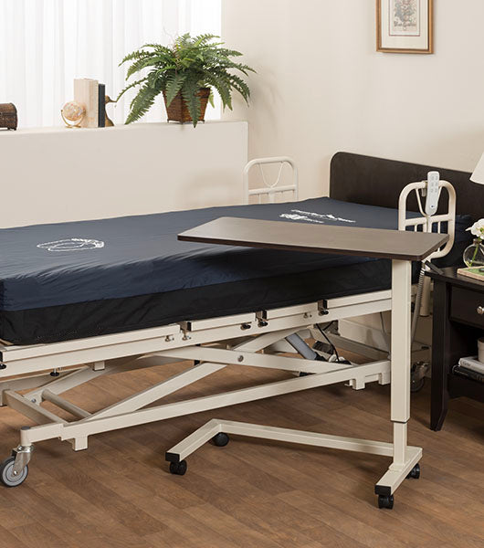 Adjustable overbed table in healthcare room setting with dark surface positioned over patient bed