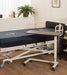 Adjustable overbed table in healthcare room setting with dark surface positioned over patient bed