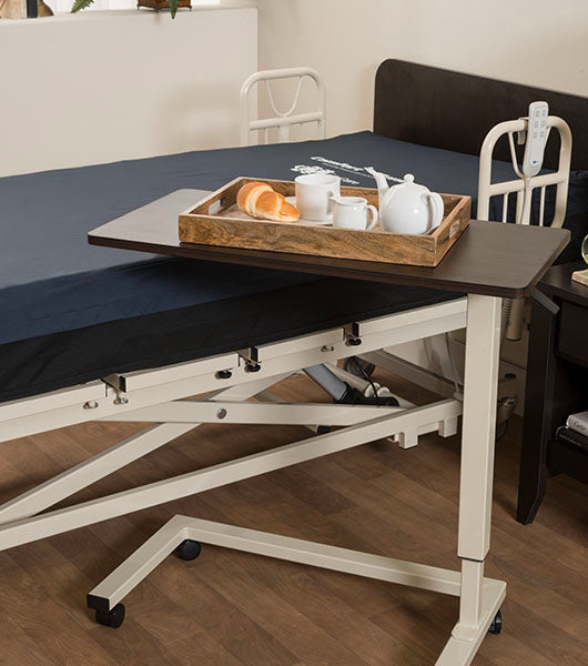 Adjustable overbed table with Mahogany surface positioned over hospital bed with meal tray