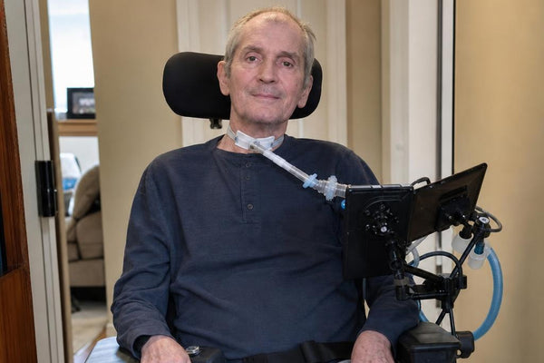 Man in a wheelchair with a tablet attached, indoors.