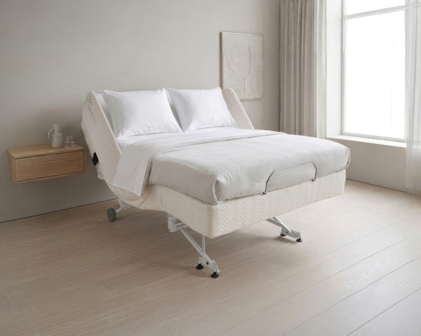 Supernal 5 adjustable hospital bed in a minimalist room with a window and wooden side table.