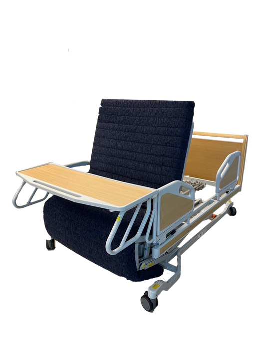 The ReNuCare Standing Bed is a 4-position adjustable hospital bed with metal rails, wood headboard and footboard, and tray table. Set upright on a wood-patterned floor, it offers enhanced comfort and support.