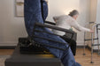 An older woman uses a walker to stand up from the UPbed Independence Adjustable Bed for Seniors by Journey Health in a living room, emphasizing fall prevention and safe mobility at home.
