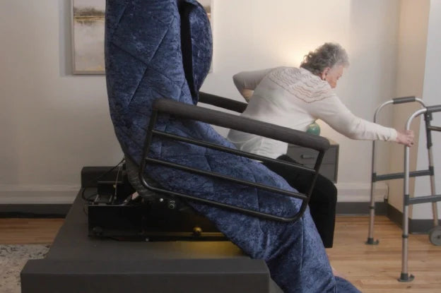 An older woman uses a walker to stand up from the UPbed Independence Adjustable Bed for Seniors by Journey Health in a living room, emphasizing fall prevention and safe mobility at home.